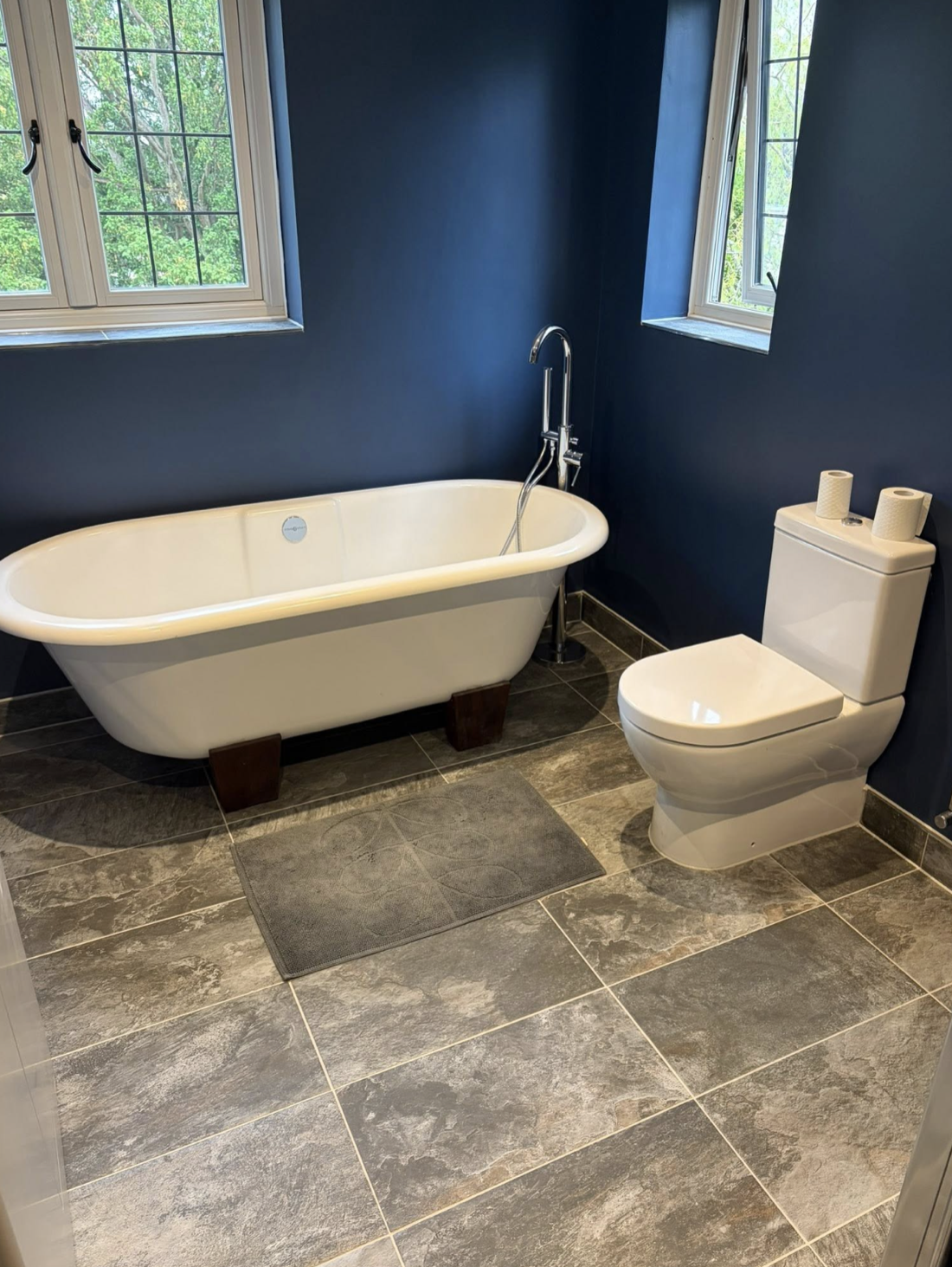 Recently completed bathroom with a freestanding bath, navy walls and slate-effect tiled floor