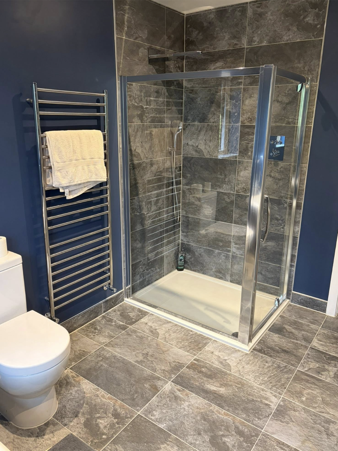 Walk-in shower enclosure with slate-effect tiling and a chrome heated towel rail